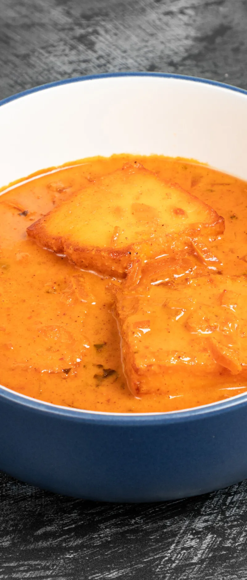 Cubes of paneer cheese immersed in a vibrant orange curry sauce with specks of herbs