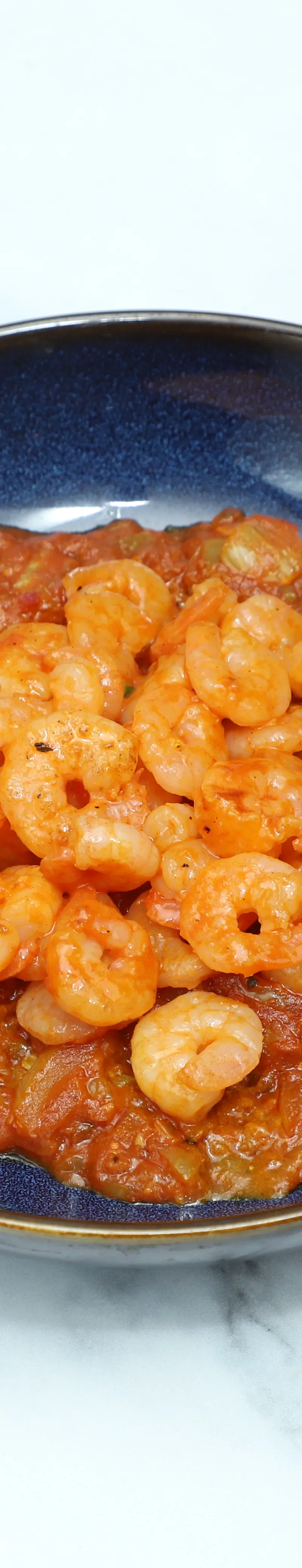 Small shrimp in a vibrant red curry sauce, served in a dark blue bowl.