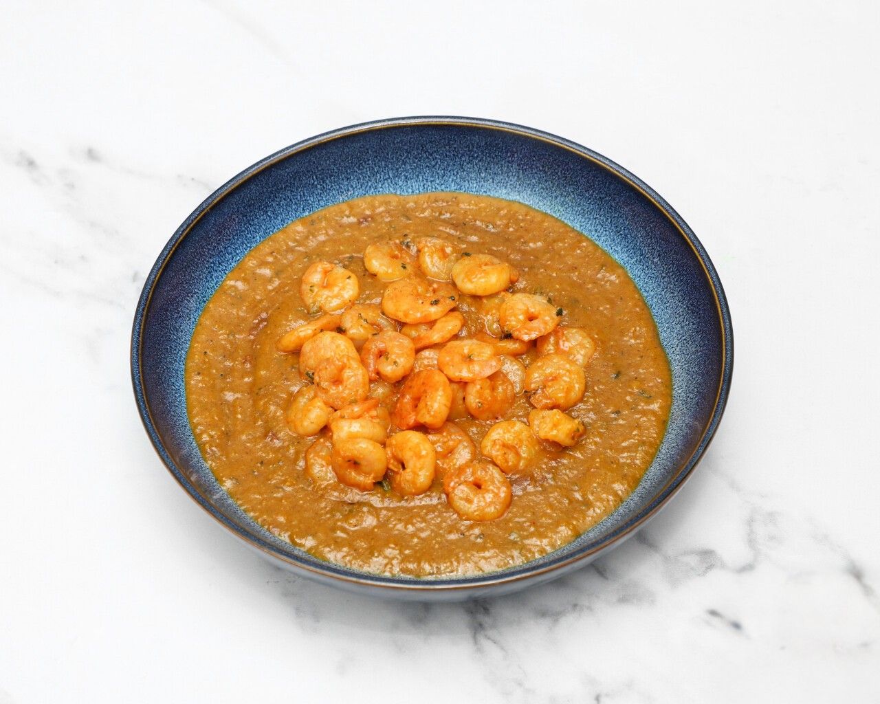Savory shrimp curry in a textured blue bowl on a white and grey marble surface.