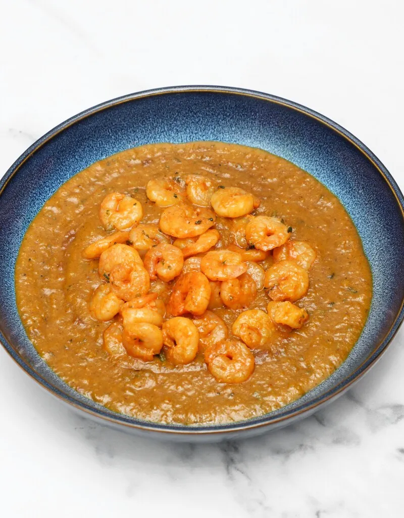 Savory shrimp curry in a textured blue bowl on a white and grey marble surface.