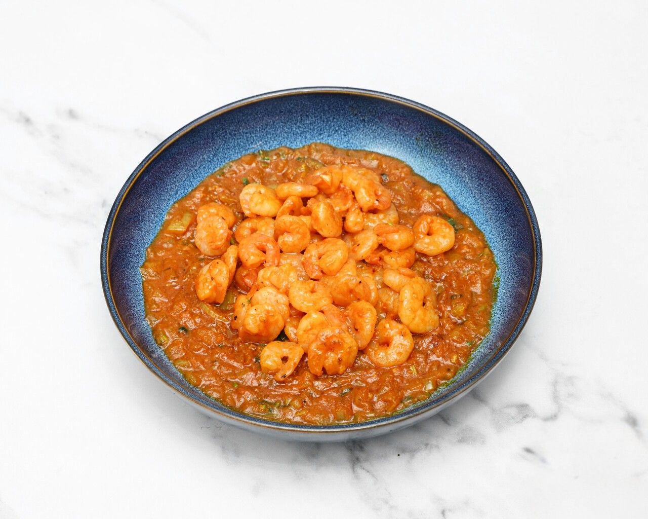 A close-up shot of King Prawn Bhoona, with prawns in a reddish-brown sauce in a blue bowl