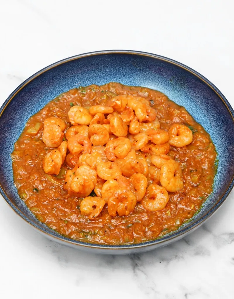 A close-up shot of King Prawn Bhoona, with prawns in a reddish-brown sauce in a blue bowl