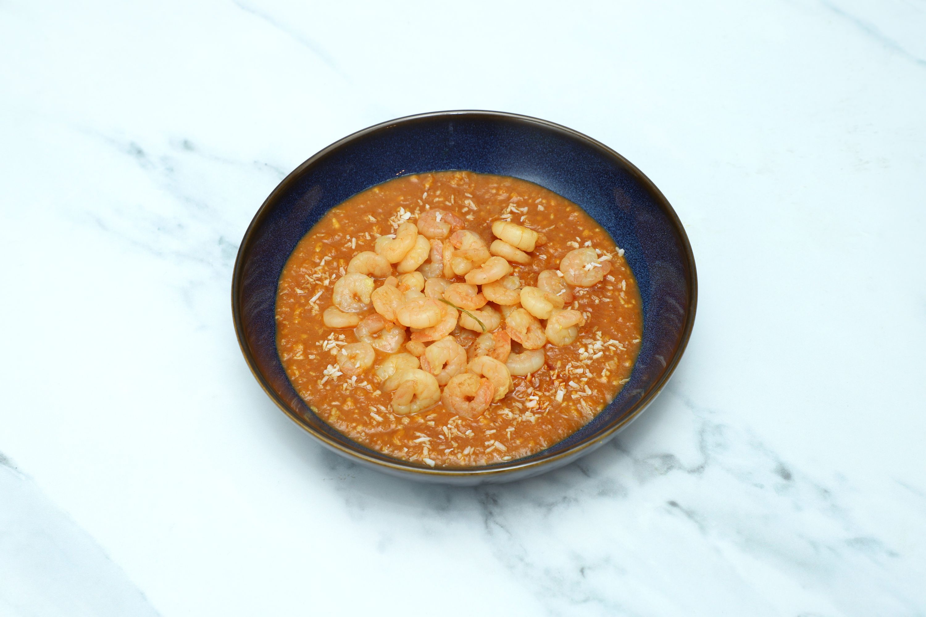 King Prawn Palok curry in a dark blue bowl, garnished with shredded coconut.
