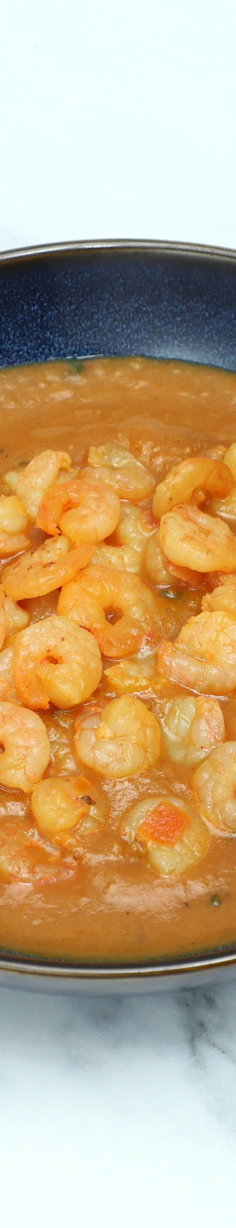 Shrimp curry with an orange-brown sauce and many small shrimp in a dark blue bowl.