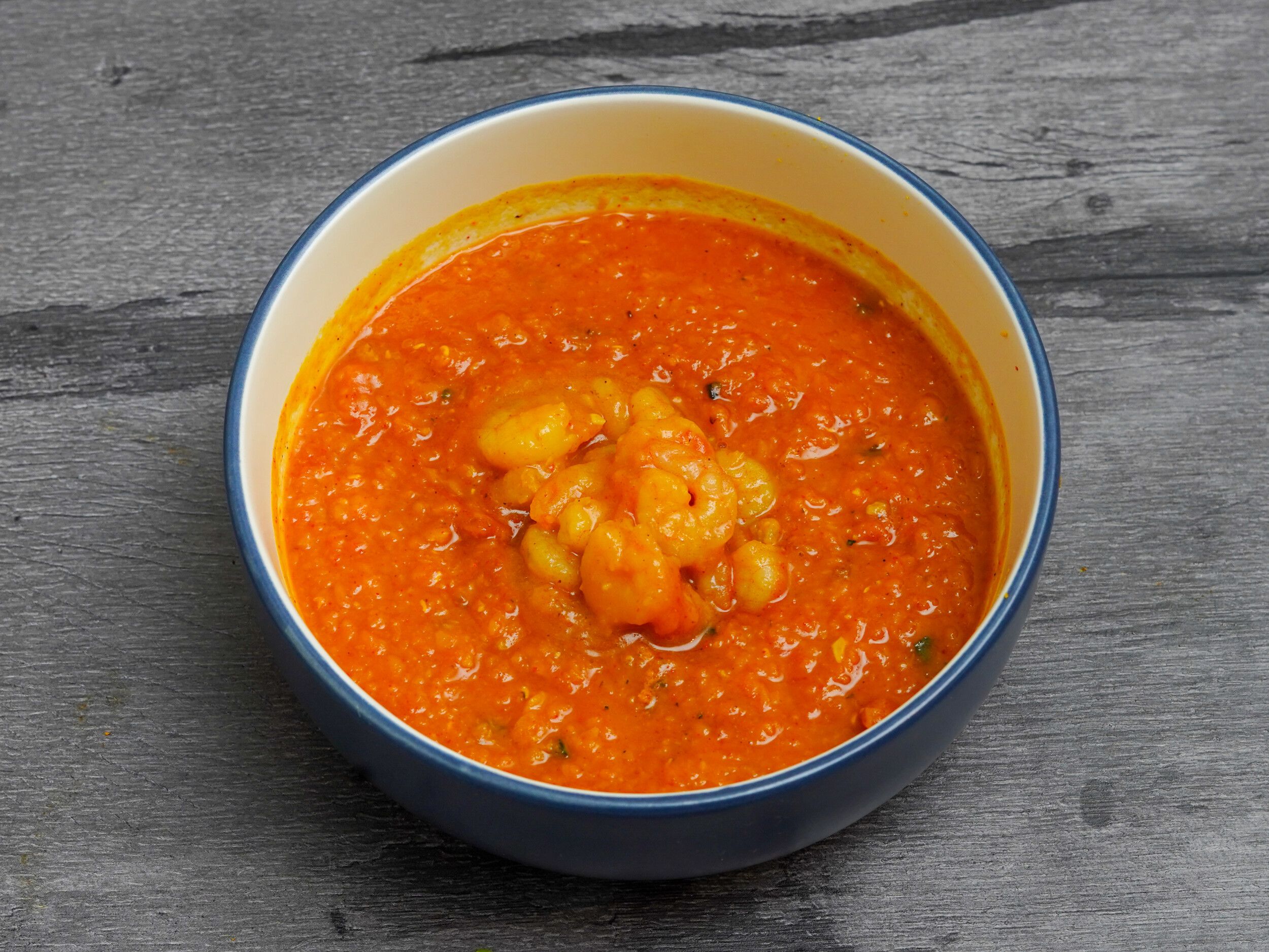 A close-up shot of a bright orange prawn curry in a white bowl with a blue rim