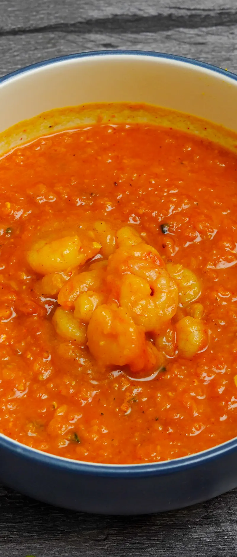 A close-up shot of a bright orange prawn curry in a white bowl with a blue rim