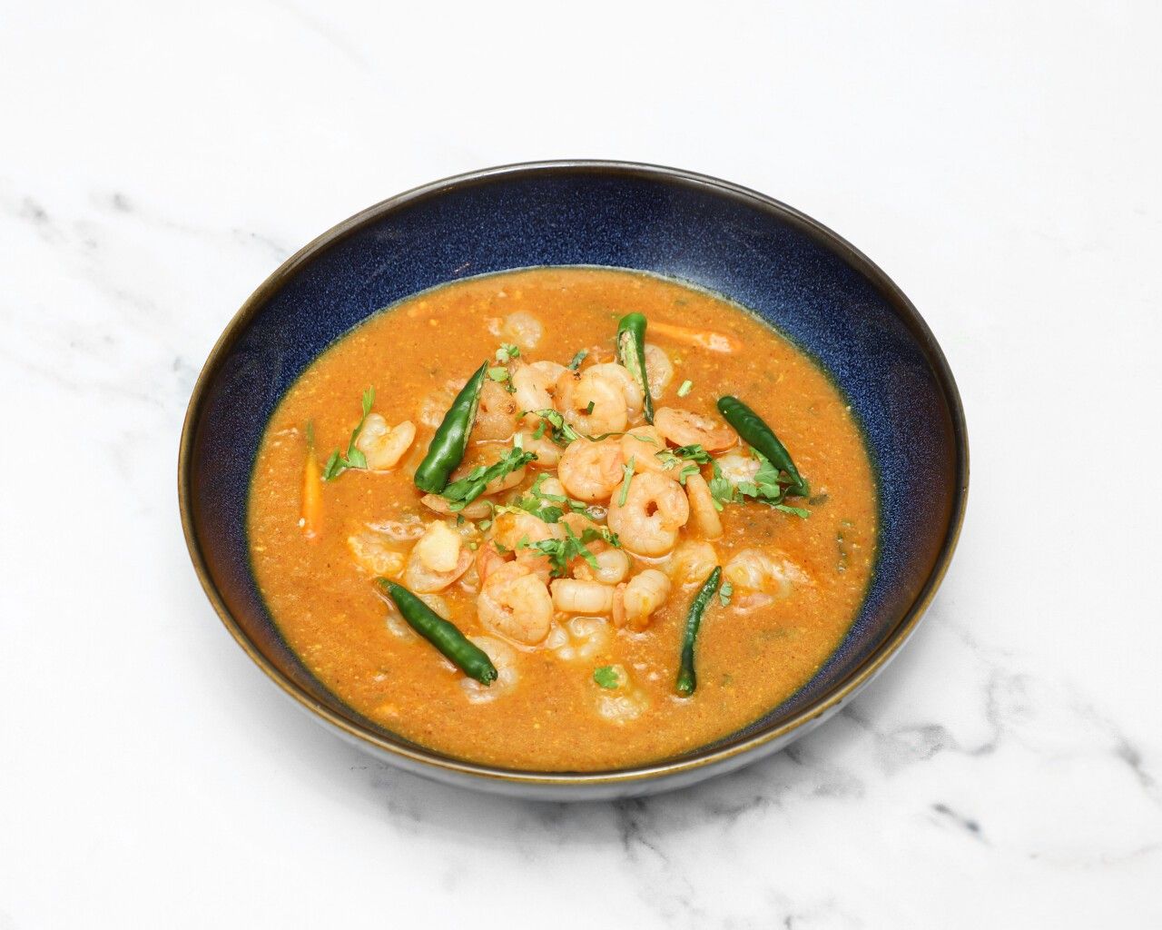 Close-up of king prawn saag curry with green chillies and coriander in a blue bowl.