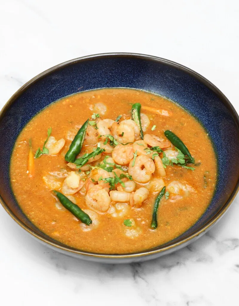 Close-up of king prawn saag curry with green chillies and coriander in a blue bowl.