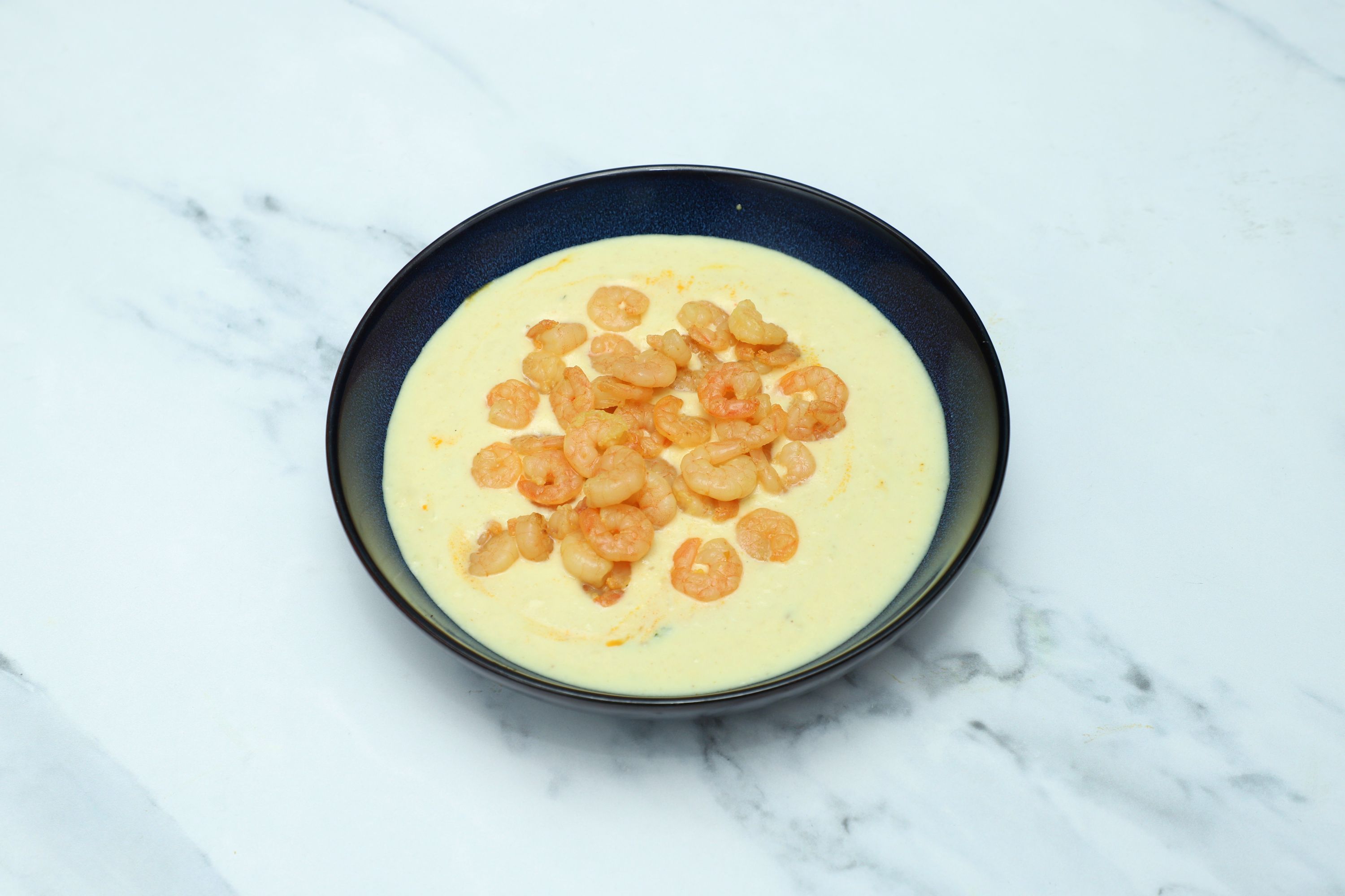 A black bowl filled with a light yellow creamy curry topped with small, cooked shrimps.