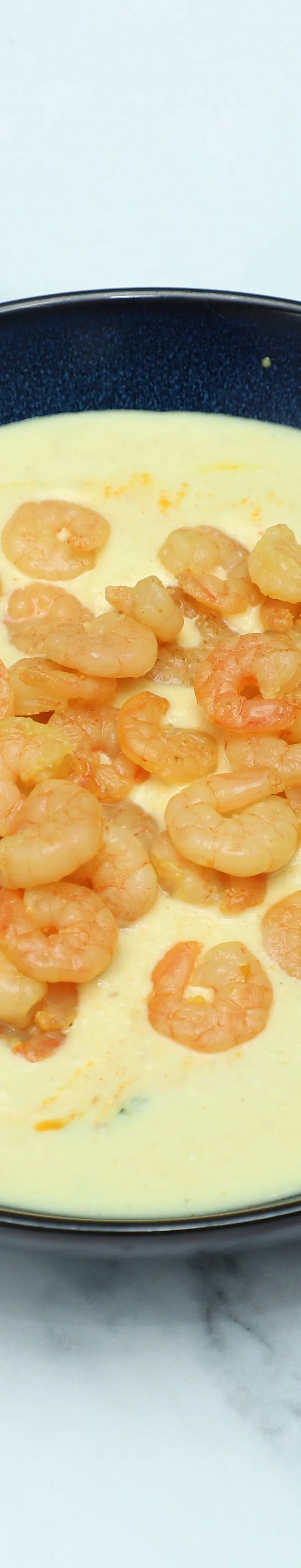 A black bowl filled with a light yellow creamy curry topped with small, cooked shrimps.