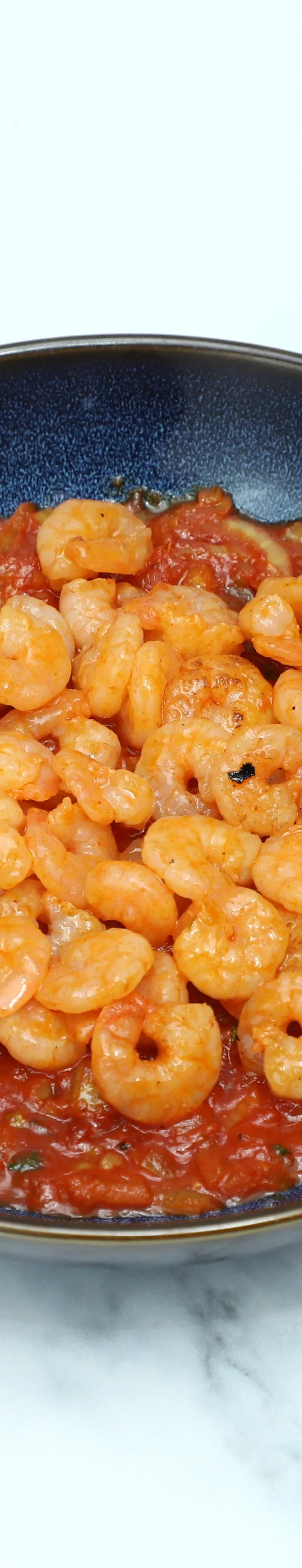 Small cooked shrimp are arranged on a deep blue bowl of red tomato curry sauce.
