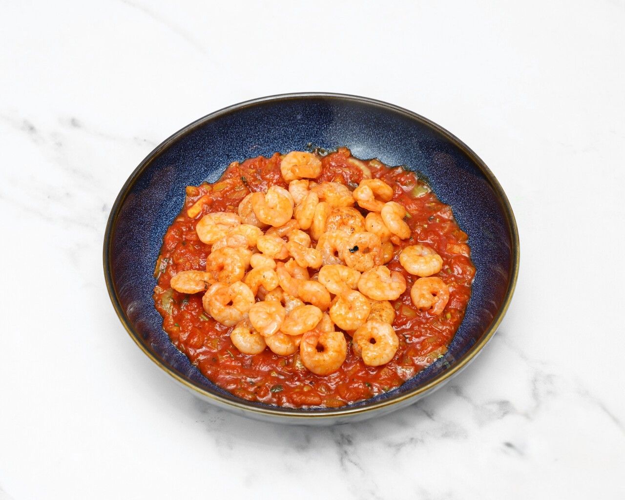 A dark blue bowl filled with small, cooked shrimp in a vibrant red tomato sauce.