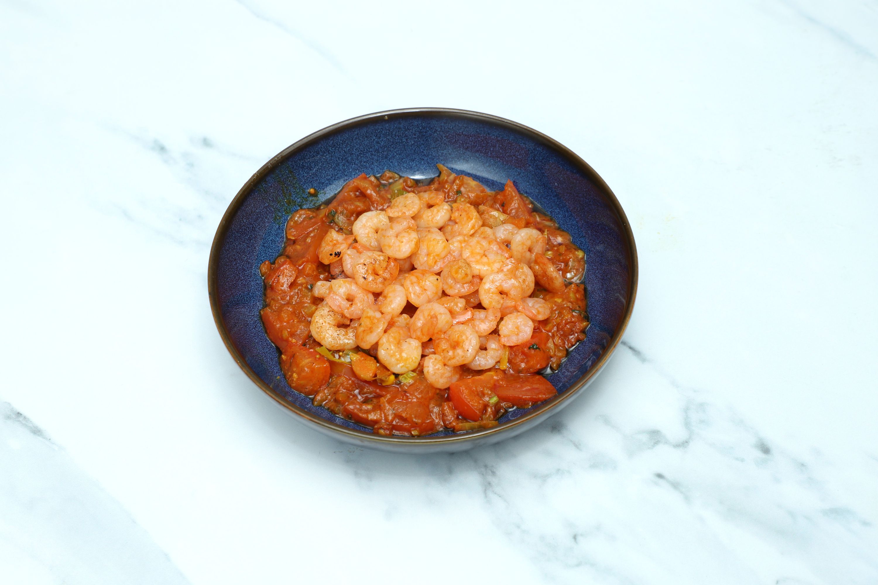 Shelled shrimp piled on top of a stewed tomato and vegetable base in a blue bowl
