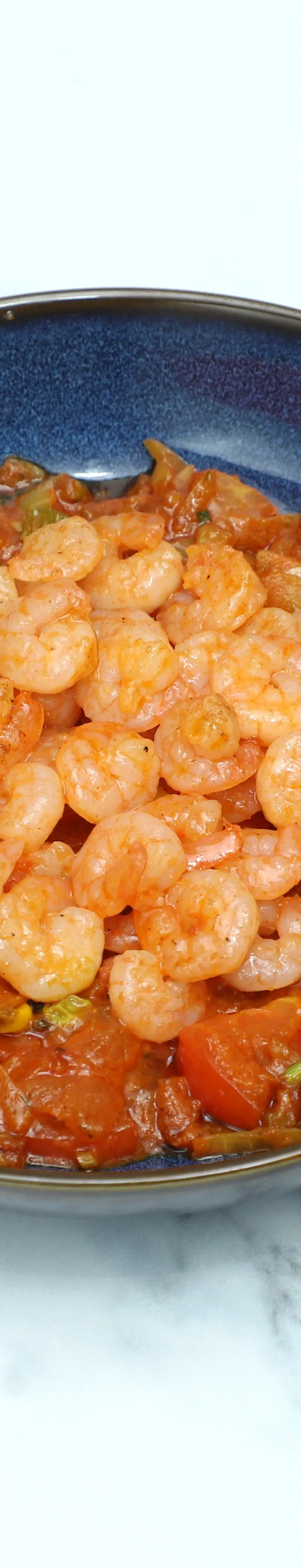 Shelled shrimp piled on top of a stewed tomato and vegetable base in a blue bowl