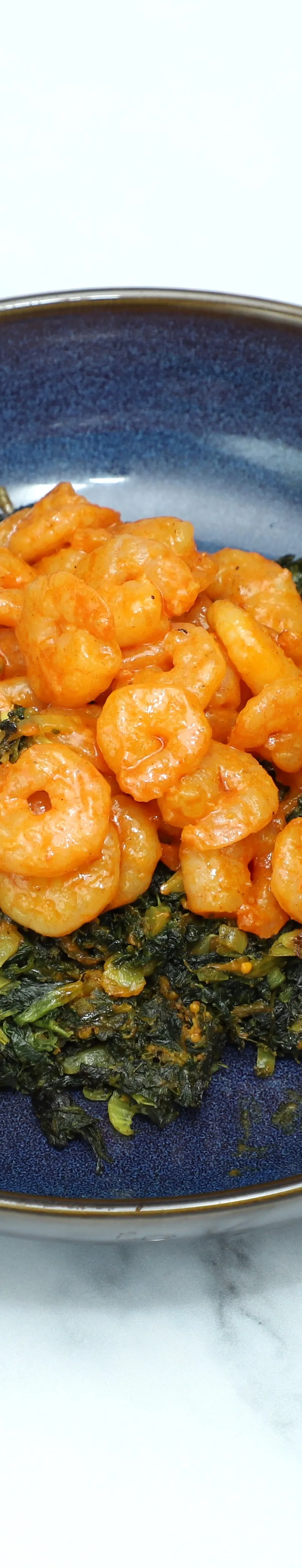 Orange shrimp curry served on top of a bed of dark green saag curry in a blue bowl