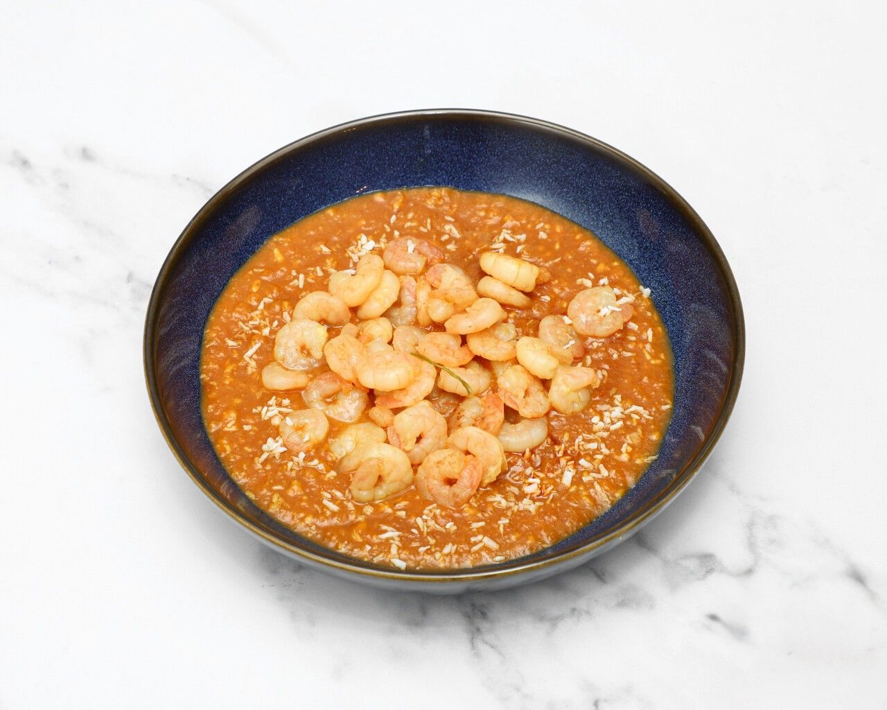 A dark blue bowl filled with orange king prawn saag, sprinkled with coconut flakes.