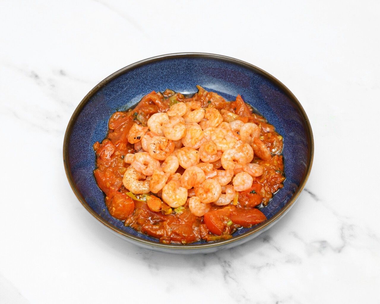 A dark blue bowl filled with a generous serving of saucy masaledar king prawns.