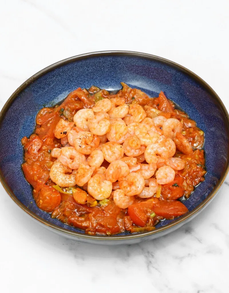 A dark blue bowl filled with a generous serving of saucy masaledar king prawns.