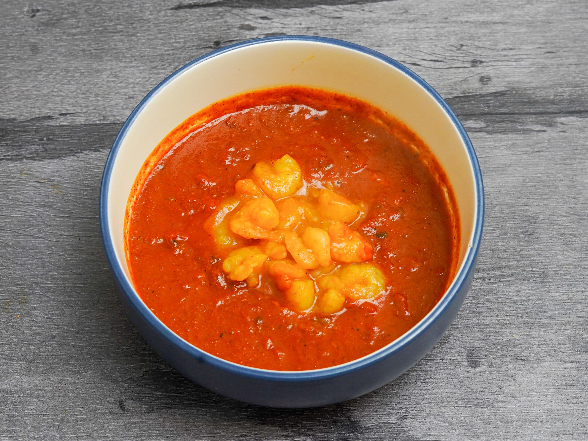 A close-up of a blue and white ceramic bowl filled with an orange-red shrimp curry.