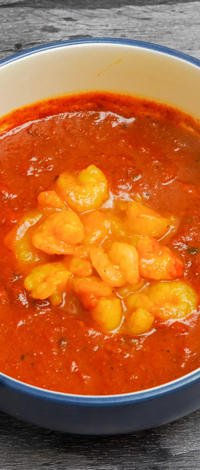 A close-up of a blue and white ceramic bowl filled with an orange-red shrimp curry.