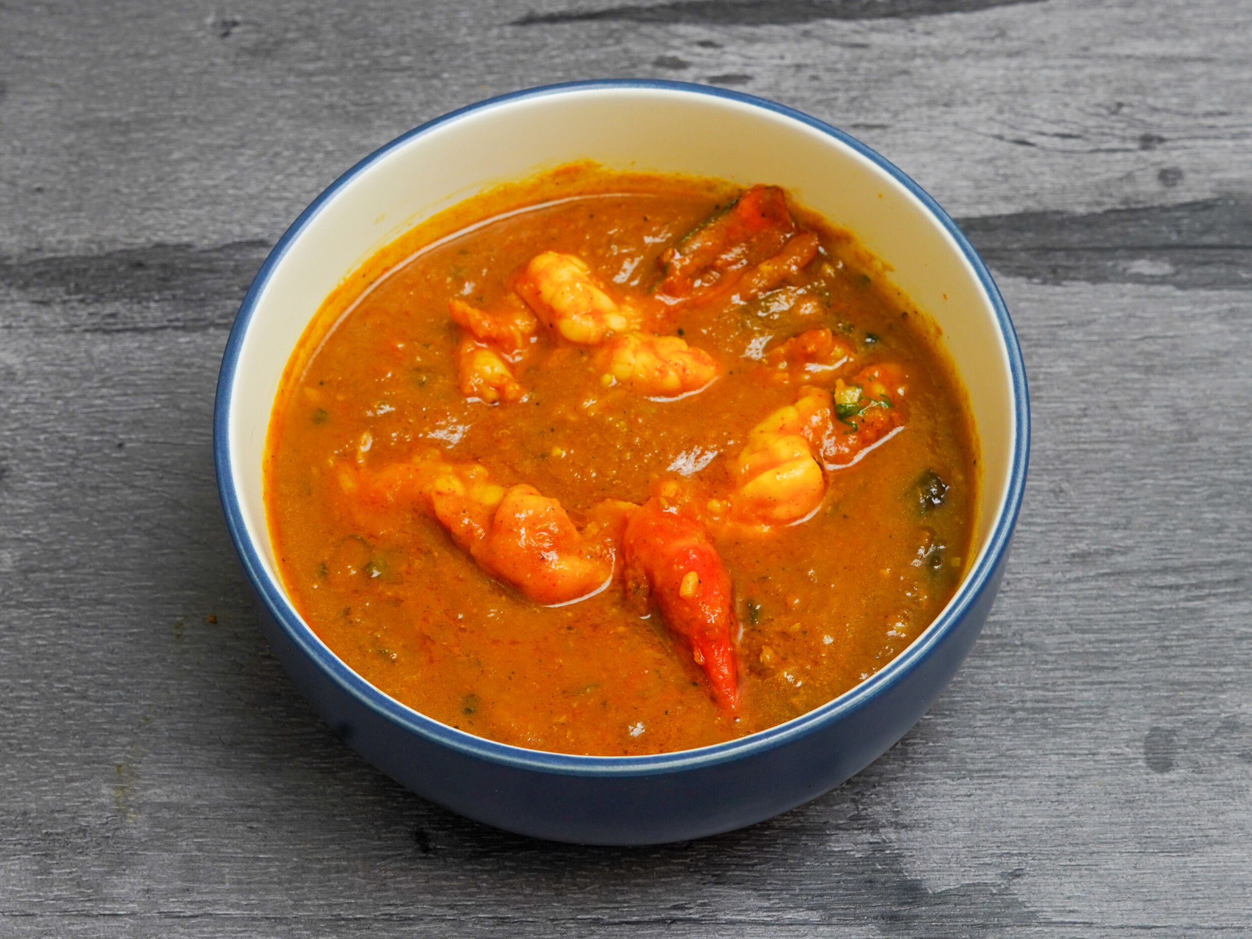 Shrimp curry in a blue and white ceramic bowl on a grey wooden surface