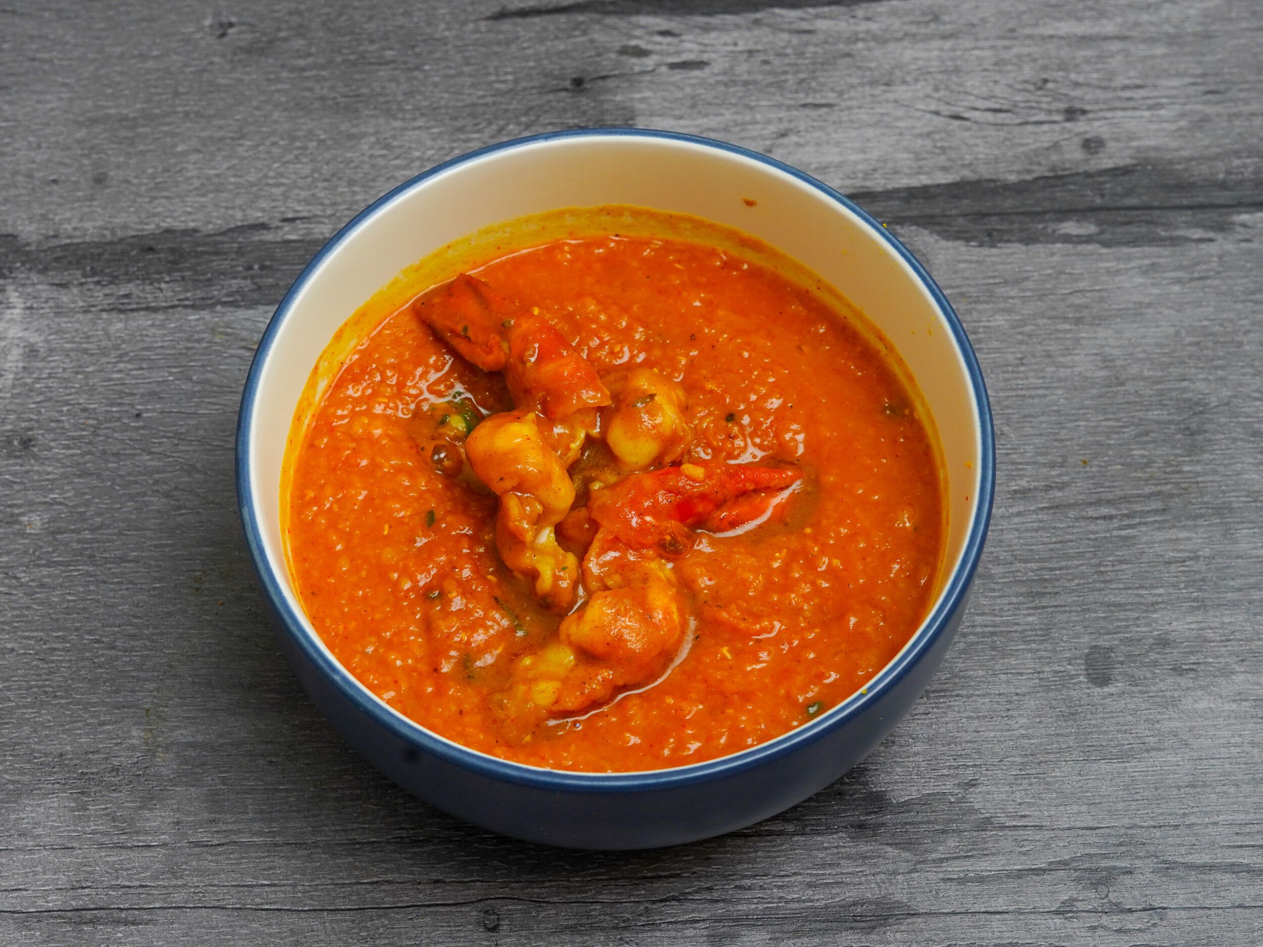 Orange-red prawn curry with visible prawns and green herbs, served in a blue and white bowl.