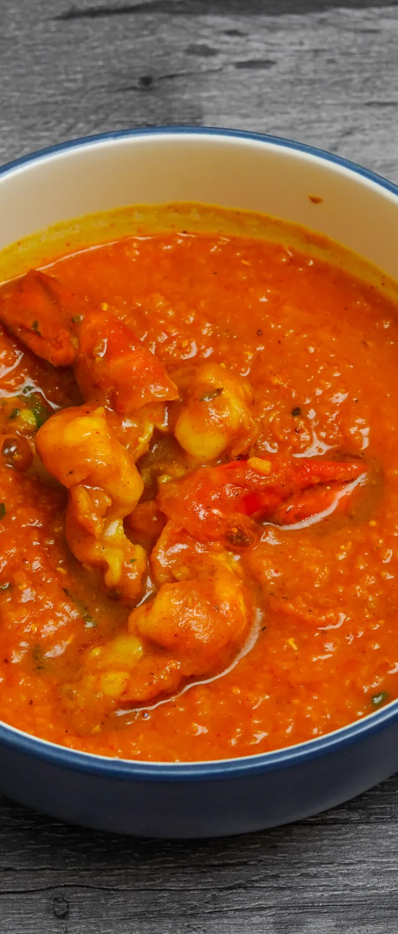 Orange-red prawn curry with visible prawns and green herbs, served in a blue and white bowl.