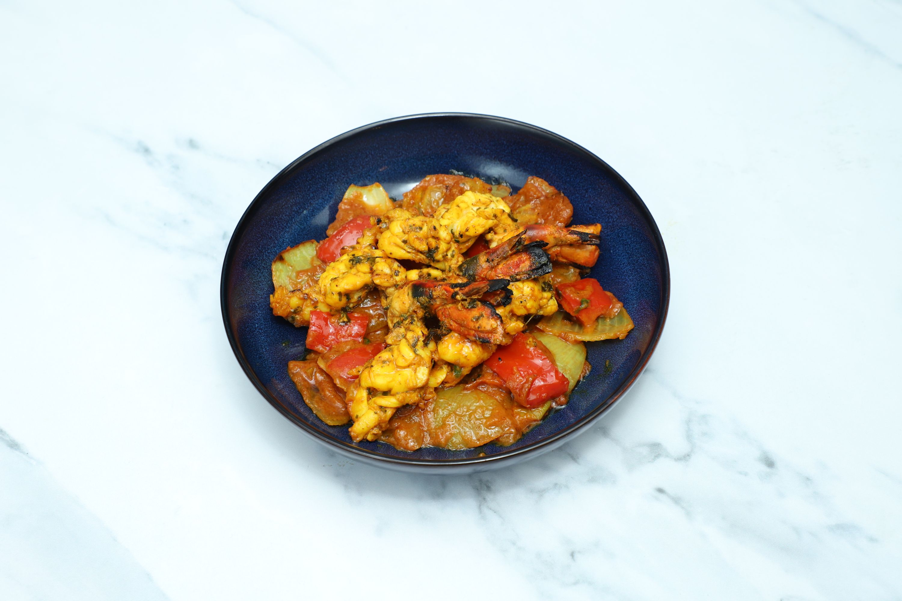Stir-fried lobster pieces and charred red bell peppers in a rich orange sauce, served in a dark blue bowl.