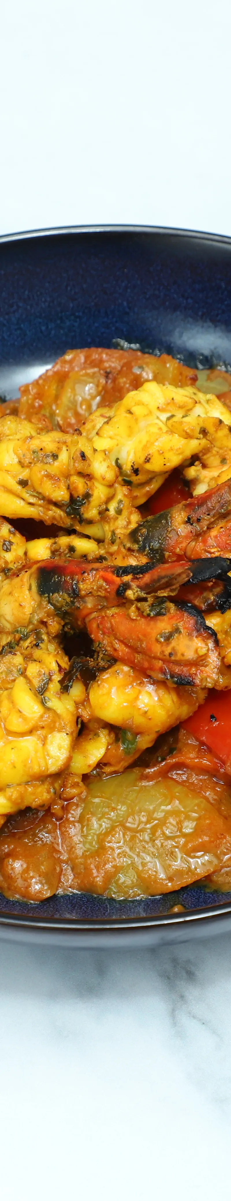Stir-fried lobster pieces and charred red bell peppers in a rich orange sauce, served in a dark blue bowl.