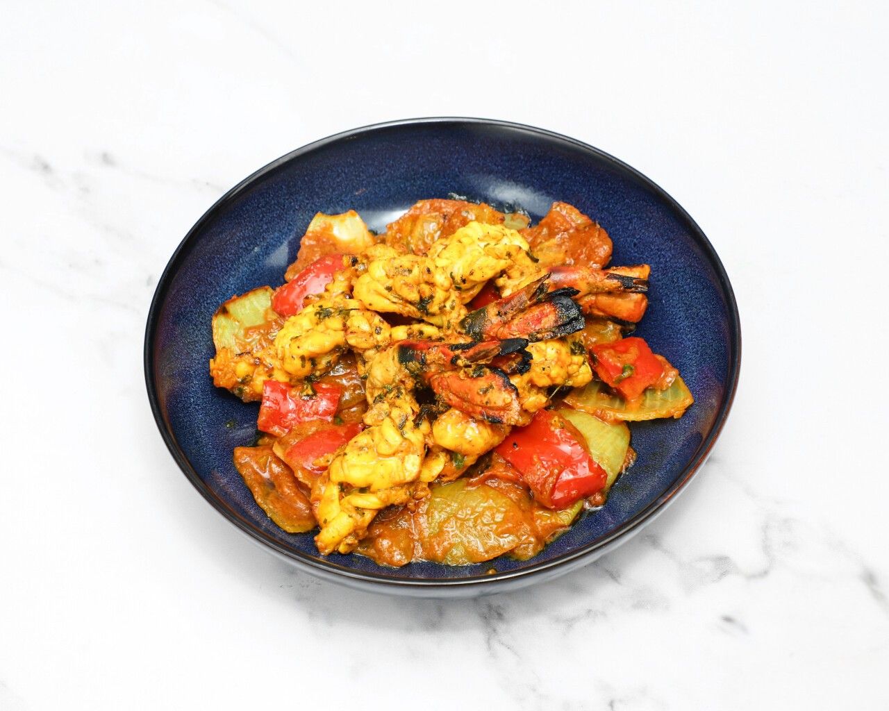 Grilled shrimp and squid with red and yellow bell peppers in a dark blue bowl
