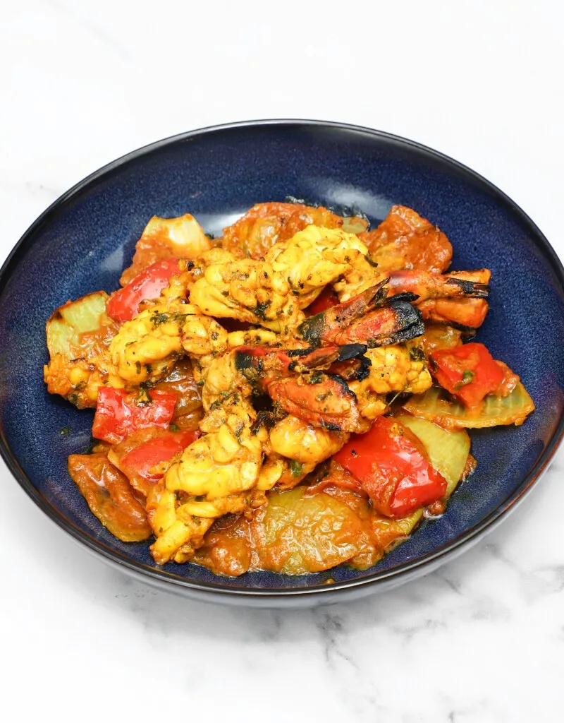 Grilled shrimp and squid with red and yellow bell peppers in a dark blue bowl