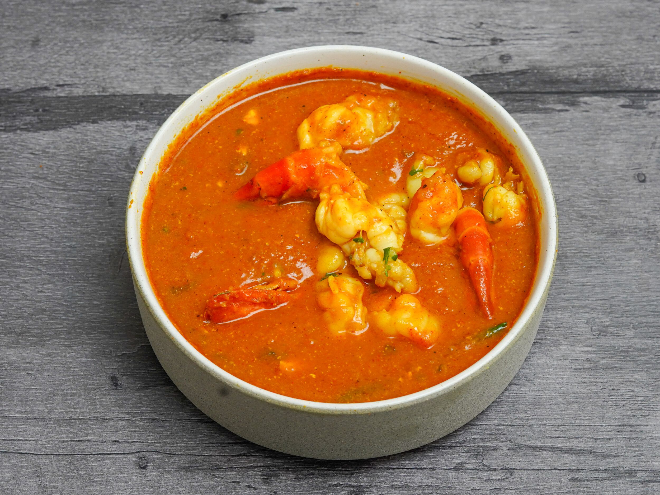 Top-down view of a light grey bowl filled with orange prawn curry on a dark grey wooden surface