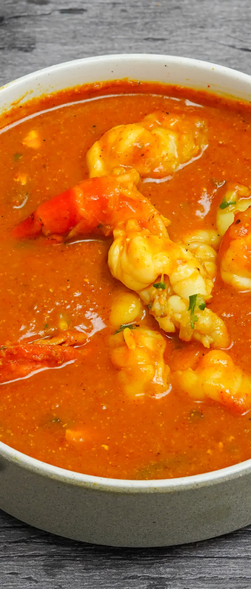 Top-down view of a light grey bowl filled with orange prawn curry on a dark grey wooden surface