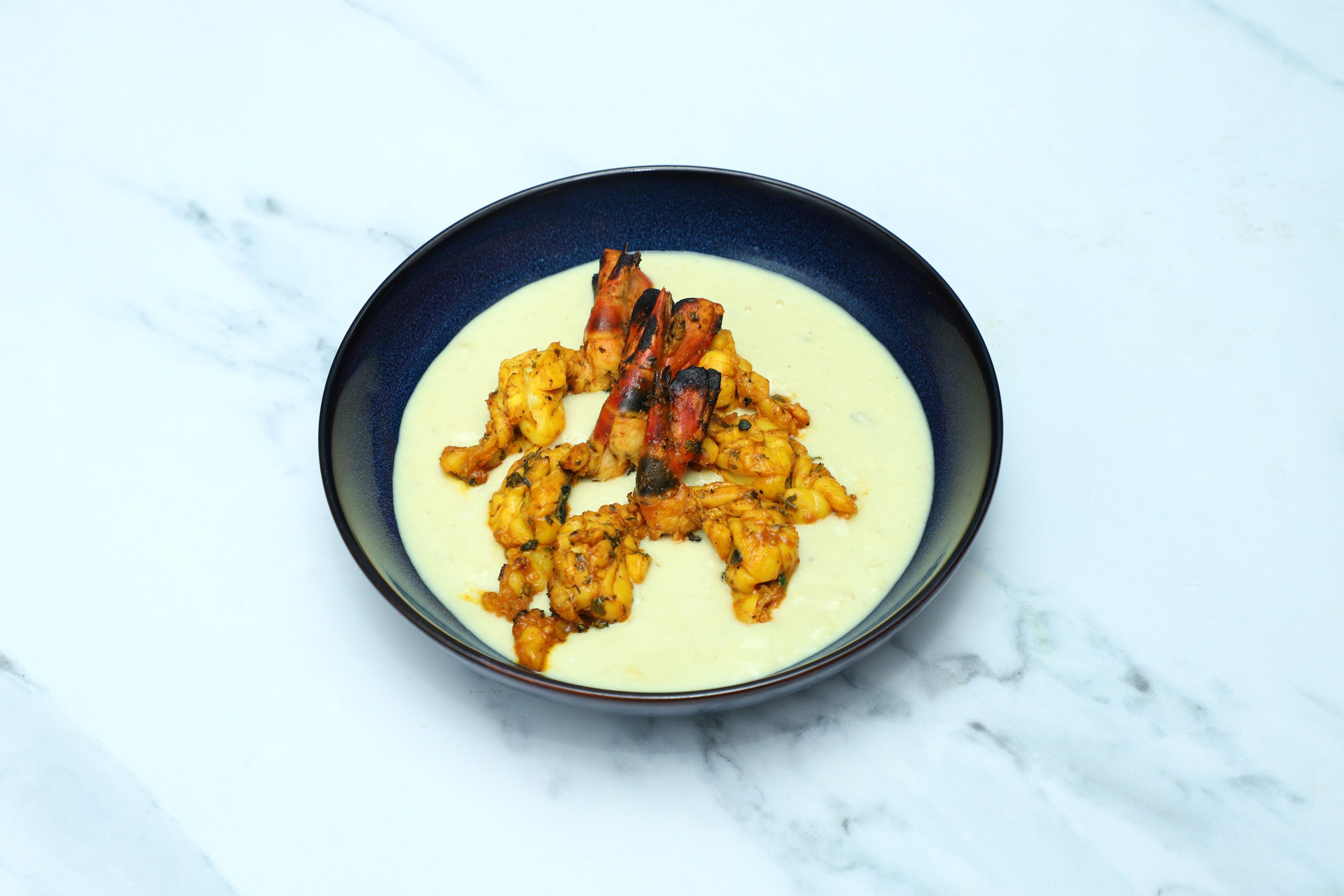 Grilled King Prawns and calamari rings in a creamy white sauce served in a dark blue bowl.