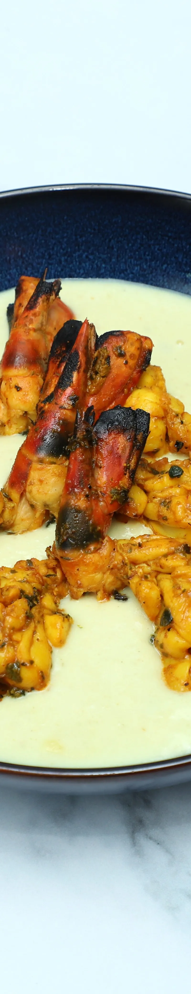 Grilled King Prawns and calamari rings in a creamy white sauce served in a dark blue bowl.