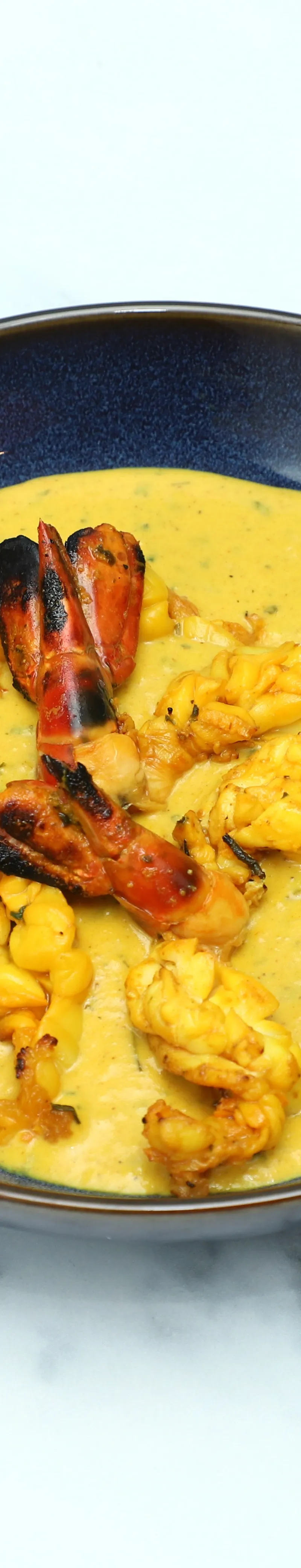 Grilled prawns with tails in a generous serving of yellow curried sauce in a dark blue bowl.