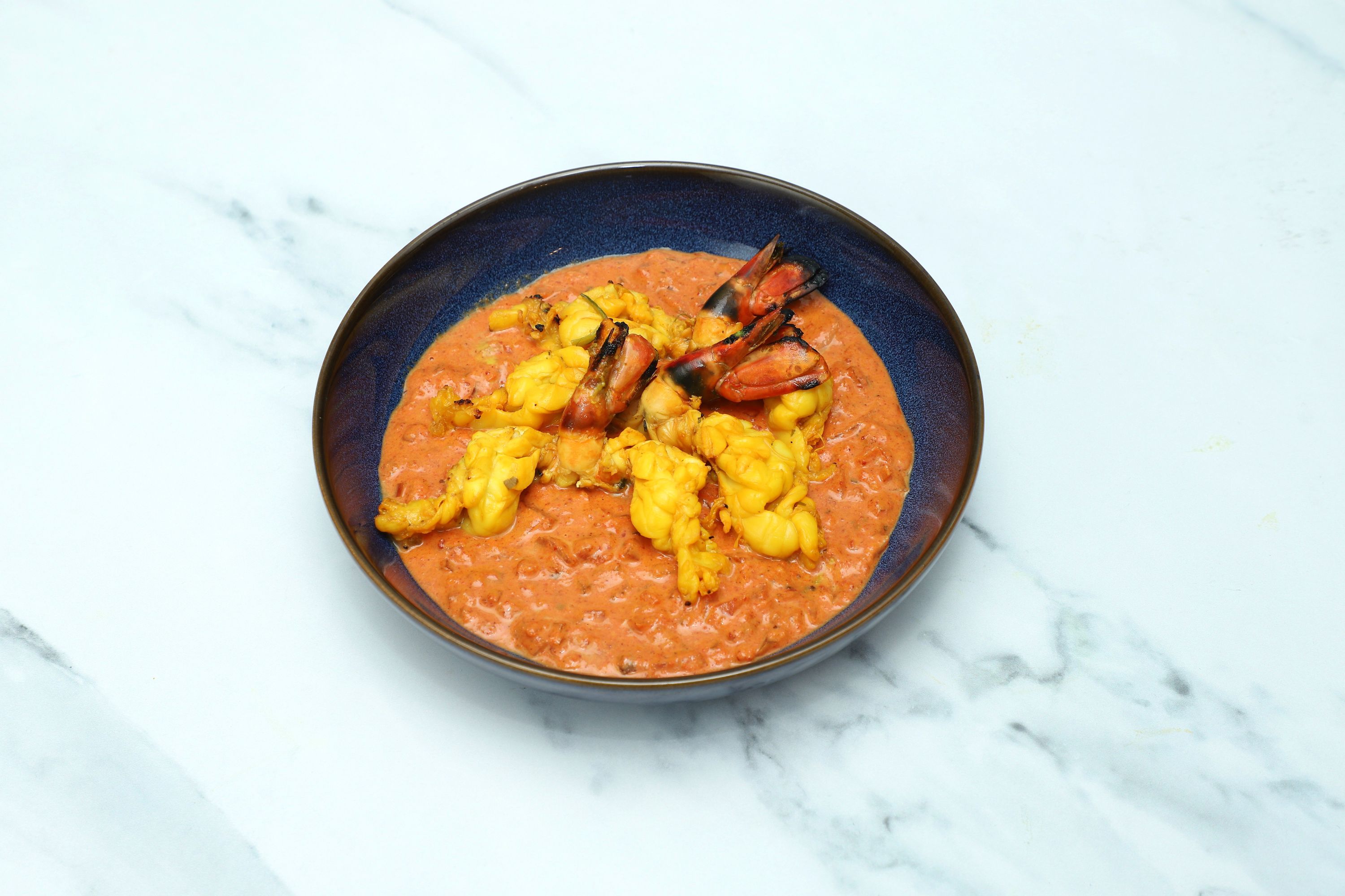 Orange curry with grilled tiger prawns and yellow monkfish pieces in a blue bowl