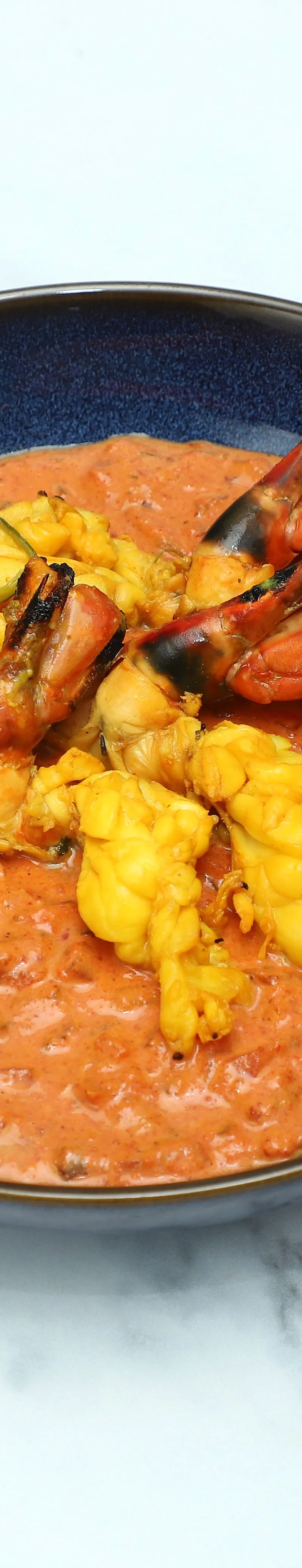Orange curry with grilled tiger prawns and yellow monkfish pieces in a blue bowl