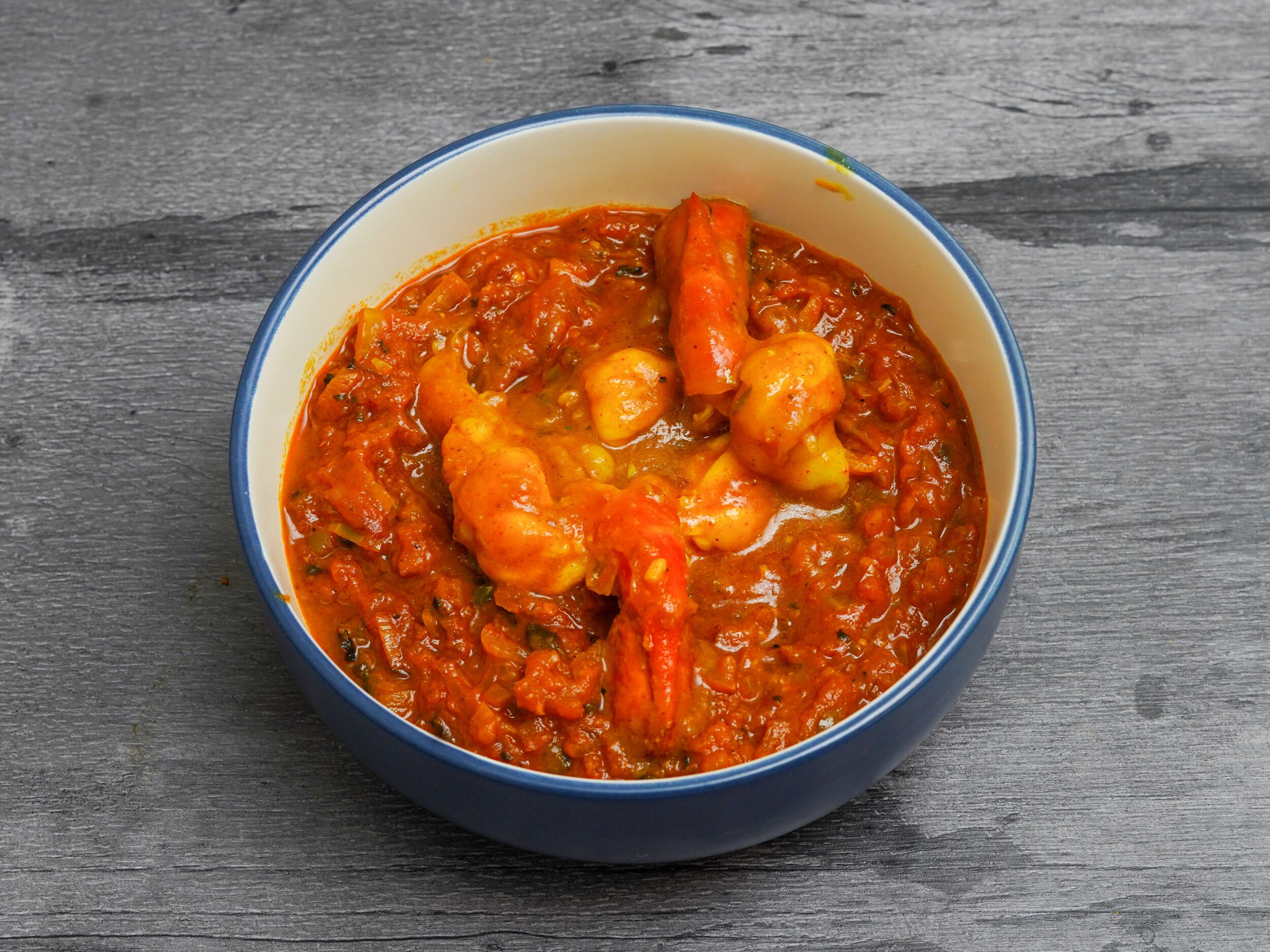 A vibrant orange shrimp curry visible in a blue and white bowl set on a gray wooden surface.