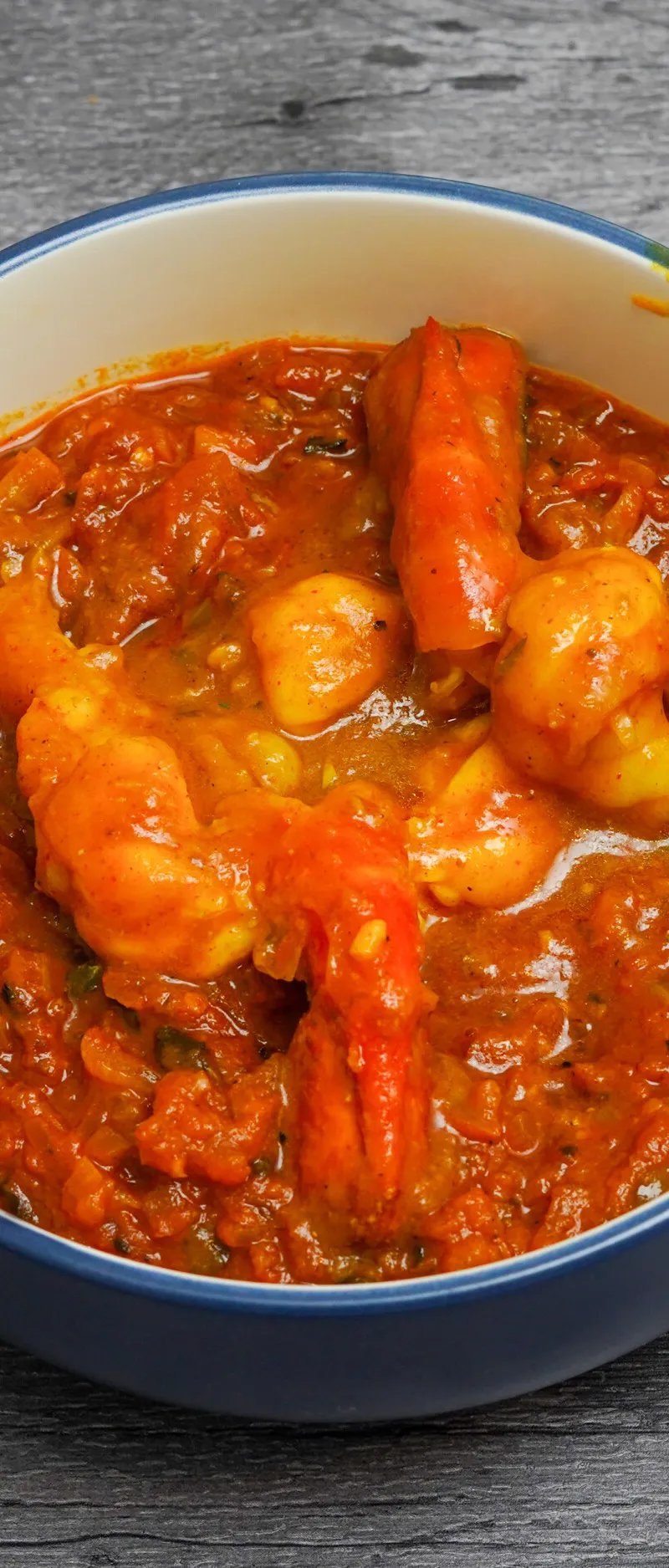 A vibrant orange shrimp curry visible in a blue and white bowl set on a gray wooden surface.