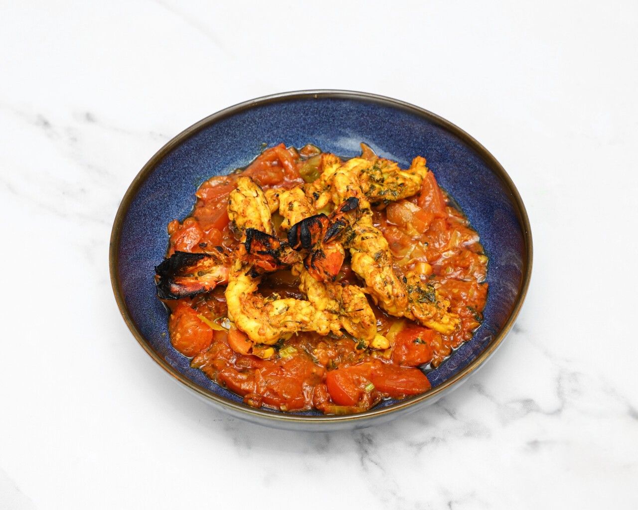Tandoori prawns with charred edges in a rich tomato-based curry in a blue bowl