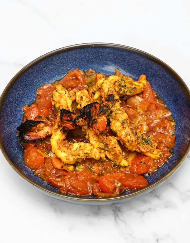Tandoori prawns with charred edges in a rich tomato-based curry in a blue bowl