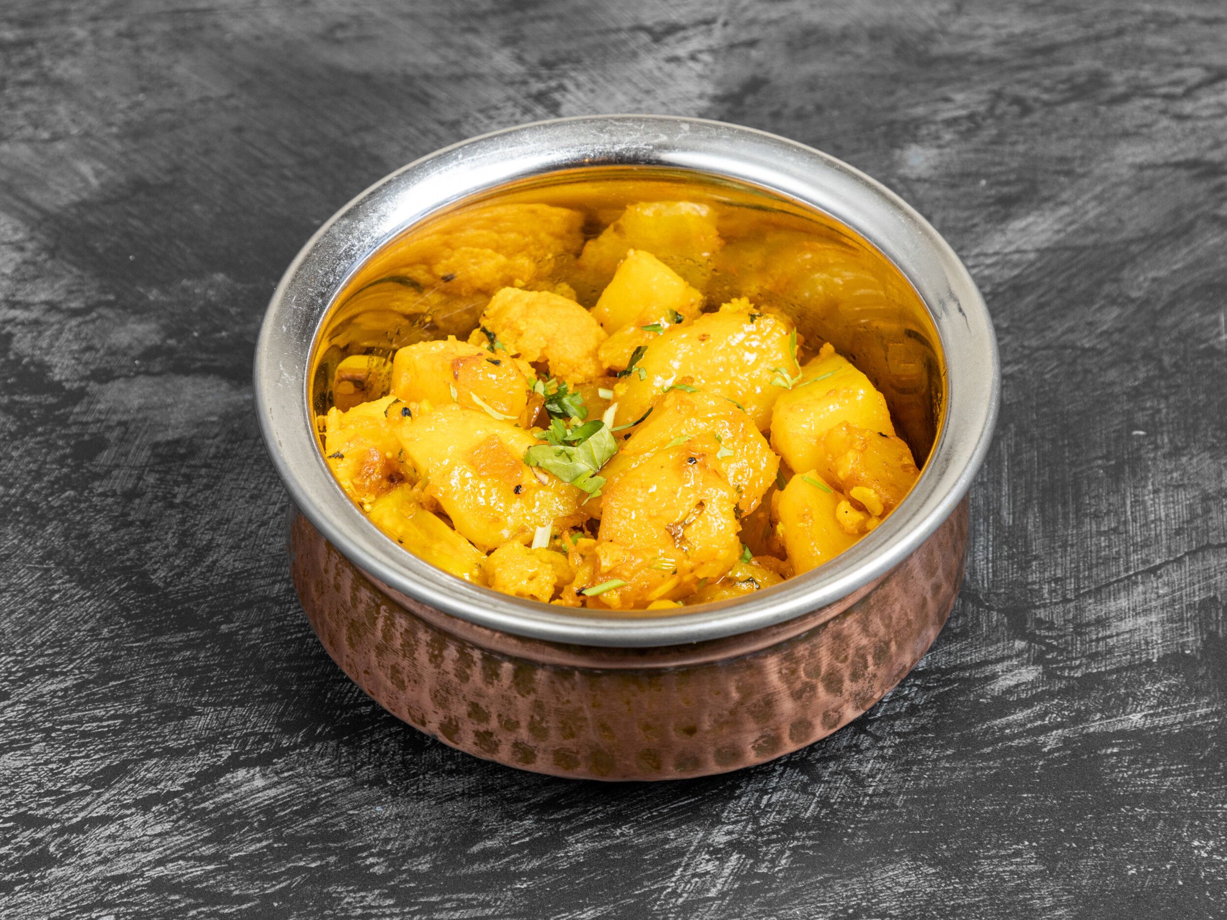 Aloo Gobi with potato and cauliflower pieces and fresh coriander in a copper karahi bowl