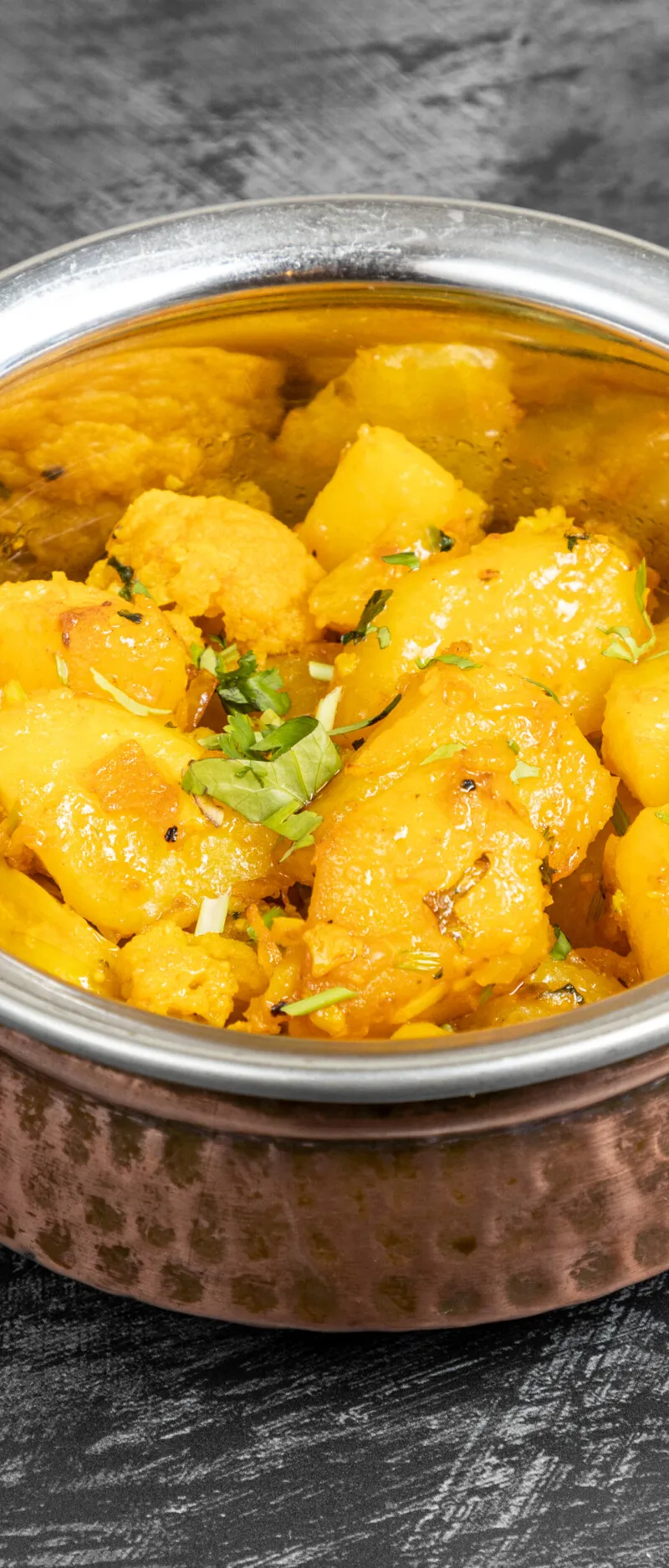 Aloo Gobi with potato and cauliflower pieces and fresh coriander in a copper karahi bowl