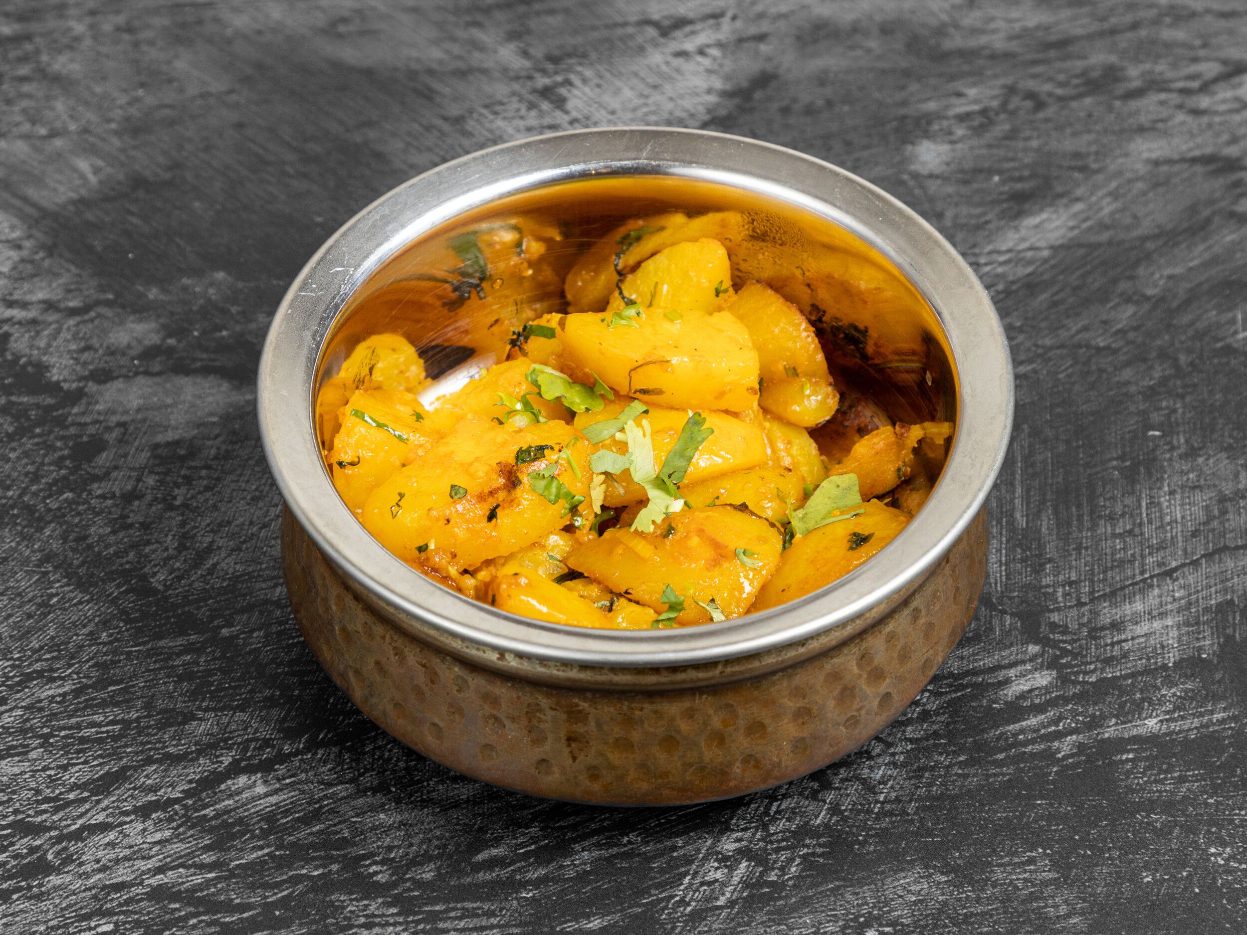 A close-up of aloo jeera, a potato and cumin stir-fry, in a copper-effect serving bowl.
