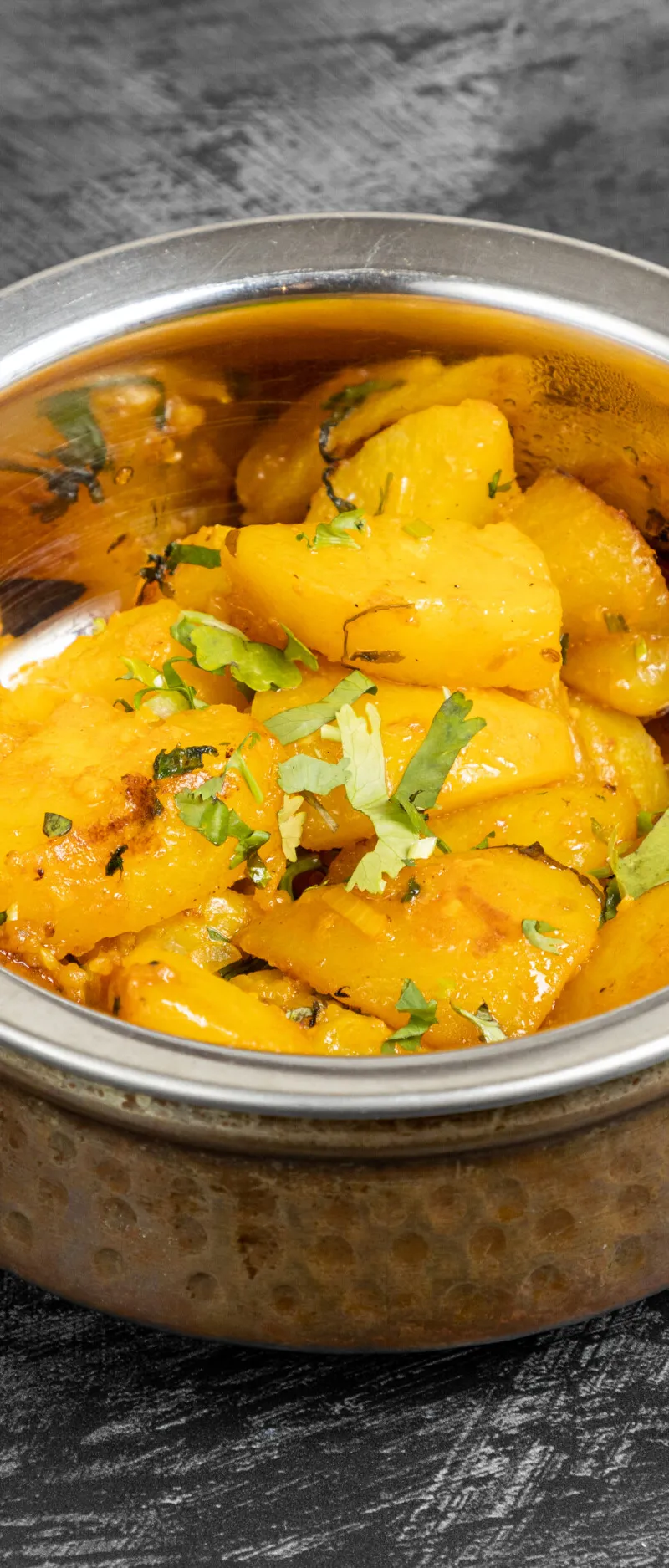 A close-up of aloo jeera, a potato and cumin stir-fry, in a copper-effect serving bowl.