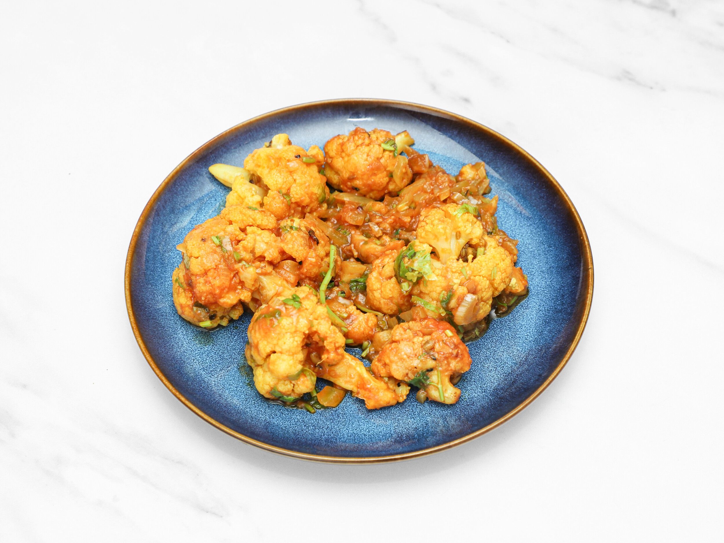 Orange-red Gobi Manchurian with visible onion and green herbs, served on a blue plate.