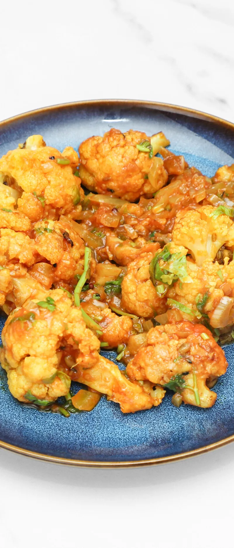 Orange-red Gobi Manchurian with visible onion and green herbs, served on a blue plate.