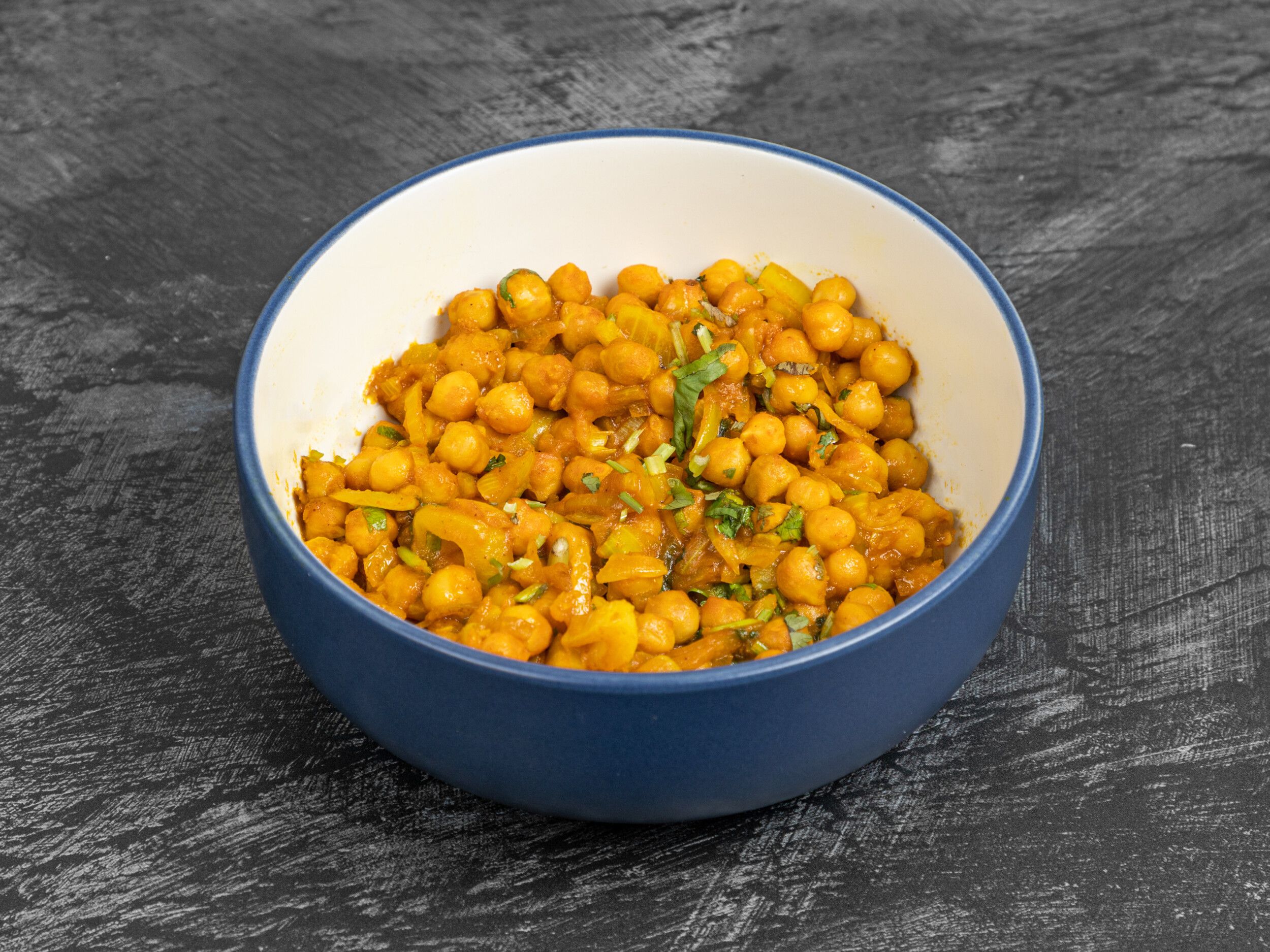 Chana masala, a chickpea curry, in a blue and white bowl against a dark grey background.