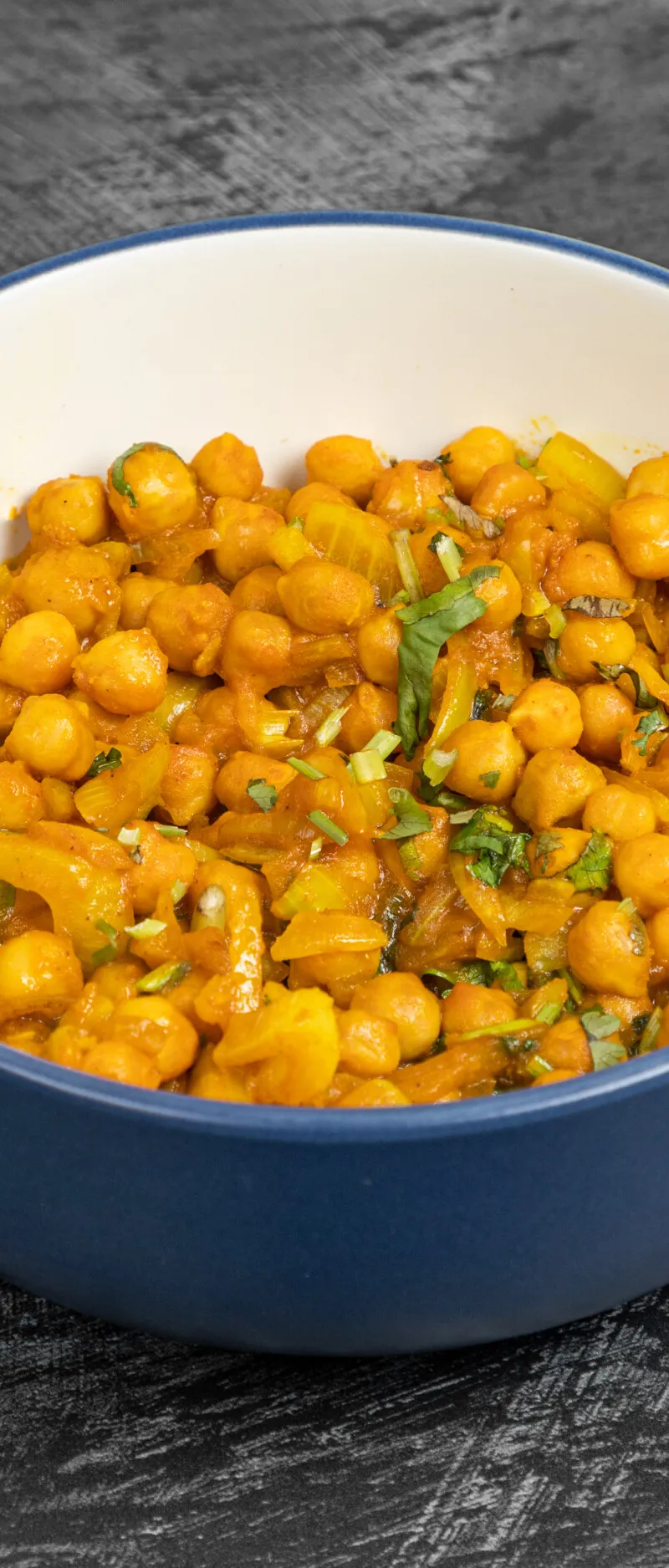 Chana masala, a chickpea curry, in a blue and white bowl against a dark grey background.
